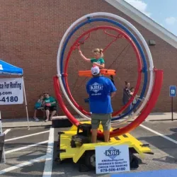  A child enjoying an amusement ride with large rings at an outdoor fair, supervised by an attendant. 