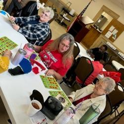Several people seated at tables, playing bingo and talking in a social setting.
