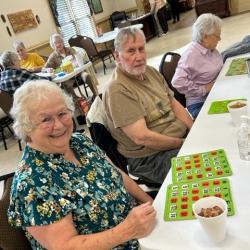 Senior women at a table, engaged in bingo, with drinks and bingo cards in front of them